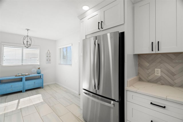 kitchen featuring freestanding refrigerator, white cabinets, light stone counters, decorative light fixtures, and baseboards