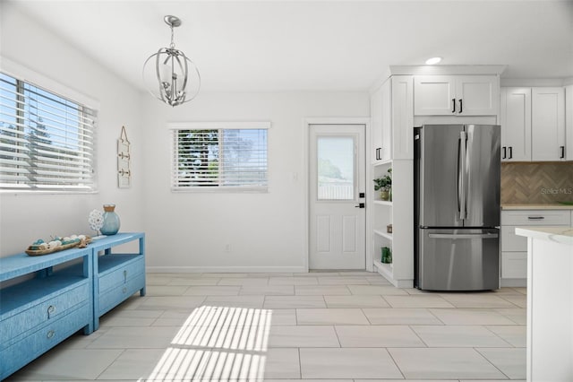 kitchen featuring baseboards, light countertops, freestanding refrigerator, white cabinets, and hanging light fixtures