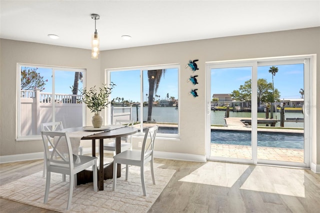 dining area featuring a water view, baseboards, and light wood-style floors