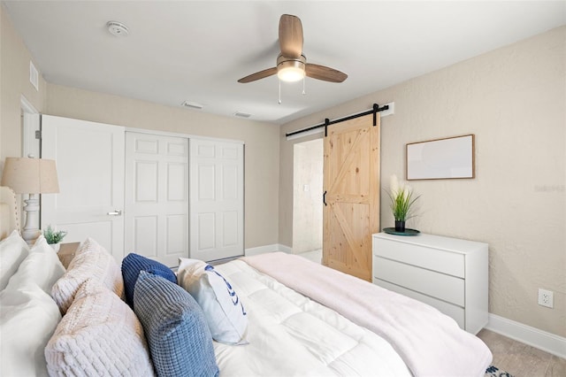 bedroom featuring a closet, a ceiling fan, a barn door, baseboards, and visible vents