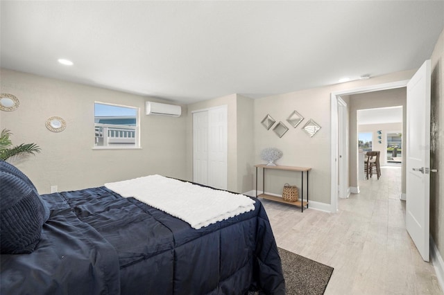 bedroom featuring baseboards, multiple windows, light wood finished floors, and a wall mounted air conditioner