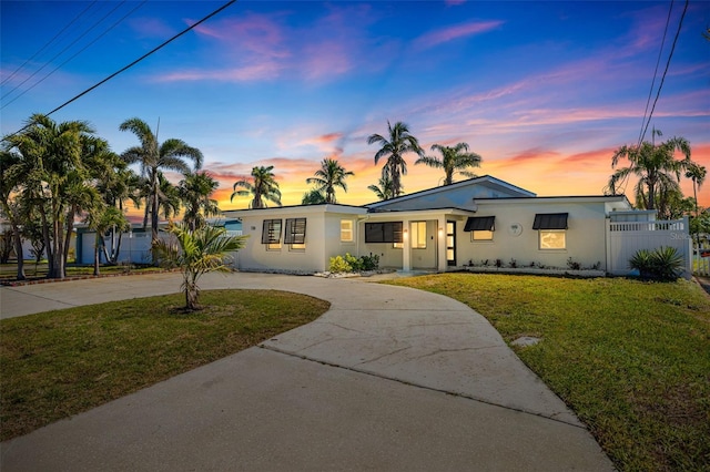 view of front of home featuring a front yard, curved driveway, stucco siding, and fence