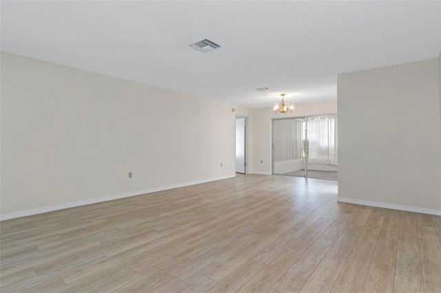 unfurnished room with baseboards, visible vents, light wood-style flooring, and an inviting chandelier