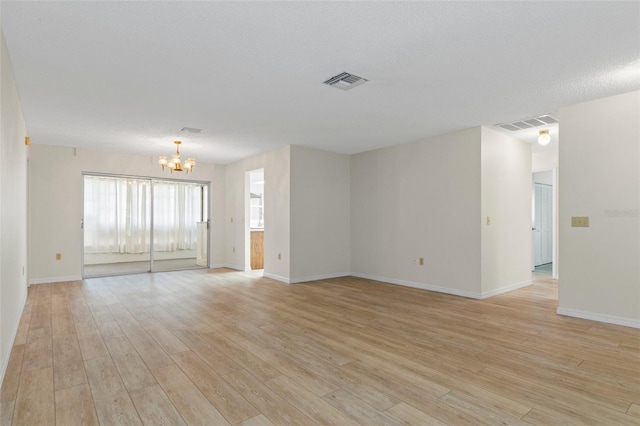 spare room with baseboards, visible vents, a notable chandelier, and light wood-style floors