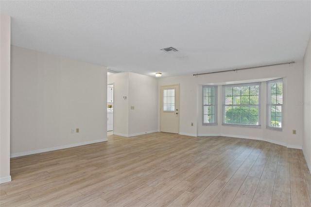 unfurnished living room with light wood-style flooring, a textured ceiling, baseboards, and visible vents