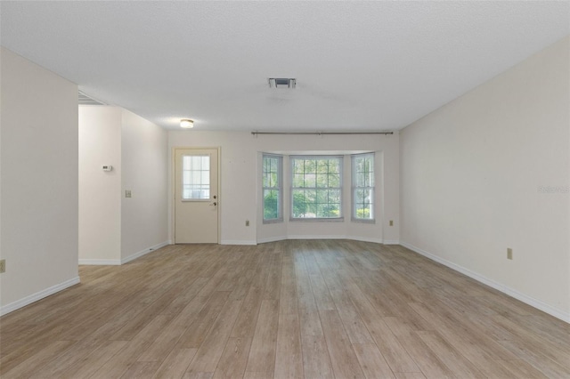 unfurnished living room with baseboards, visible vents, light wood-style floors, and a textured ceiling
