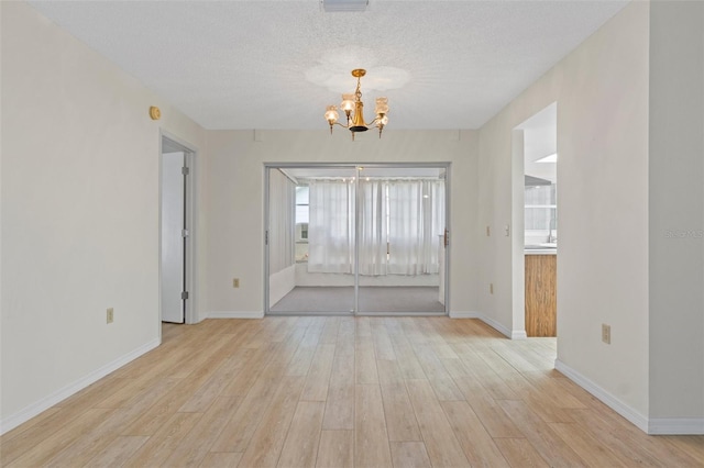 unfurnished room featuring a notable chandelier, a textured ceiling, baseboards, and light wood-type flooring