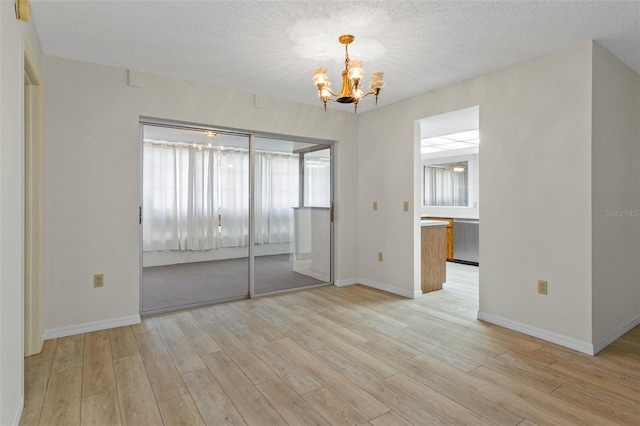 unfurnished bedroom with a textured ceiling, baseboards, a chandelier, and light wood-type flooring