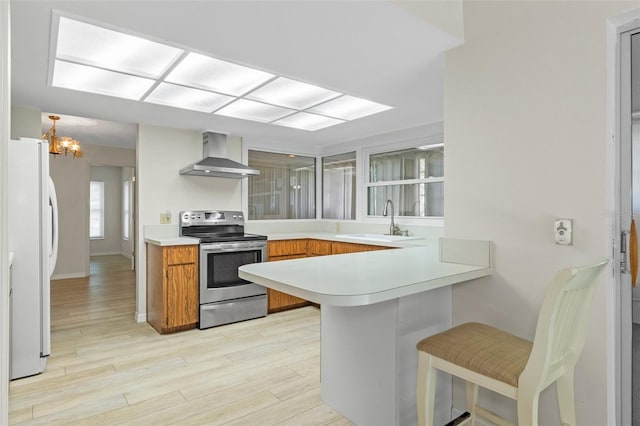 kitchen with a sink, freestanding refrigerator, wall chimney exhaust hood, a peninsula, and stainless steel electric stove