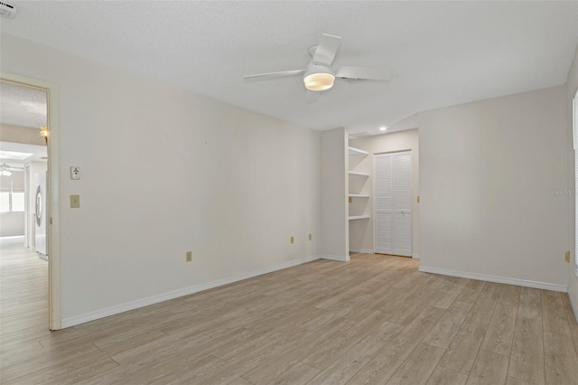 unfurnished room featuring baseboards, light wood-type flooring, a textured ceiling, and a ceiling fan