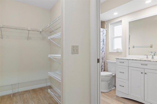 full bath featuring toilet, vanity, wood finished floors, a spacious closet, and recessed lighting