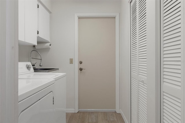 clothes washing area featuring a sink, light wood finished floors, baseboards, washer and dryer, and cabinet space
