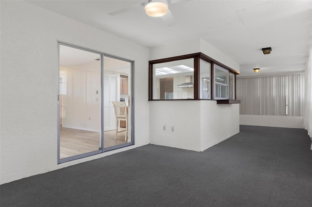 carpeted empty room featuring a textured wall and a ceiling fan