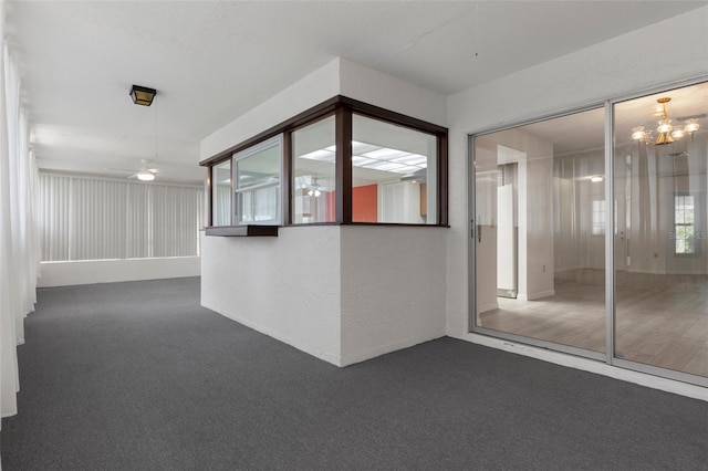 unfurnished room featuring ceiling fan with notable chandelier, dark colored carpet, and a textured wall