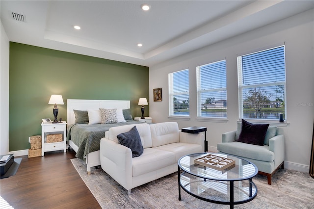 bedroom with a tray ceiling, wood finished floors, baseboards, visible vents, and recessed lighting