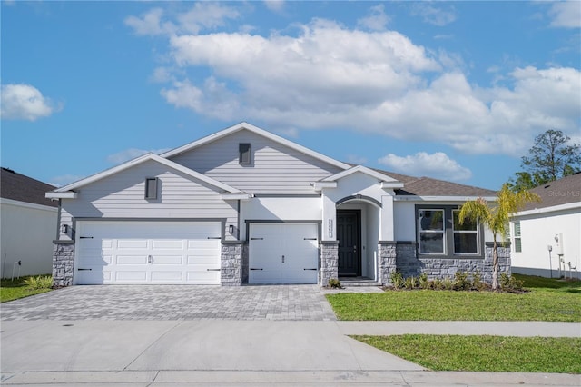 single story home featuring a front lawn, driveway, stone siding, and an attached garage