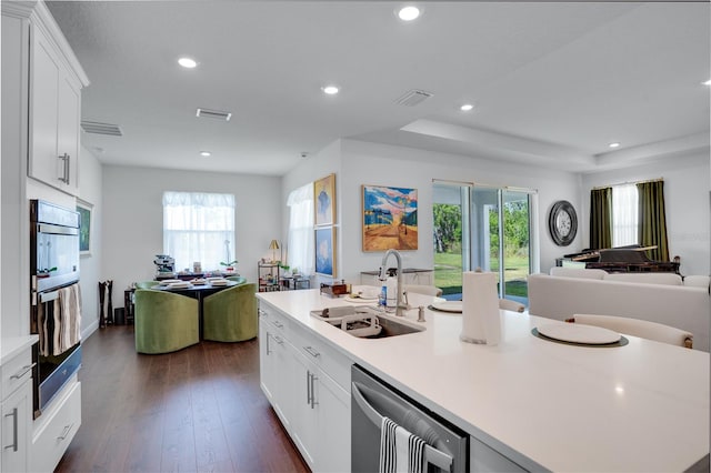 kitchen with light countertops, visible vents, a center island with sink, a sink, and open floor plan