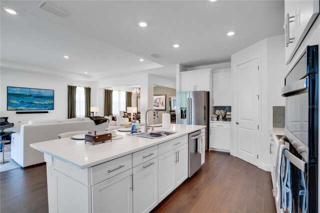 kitchen featuring appliances with stainless steel finishes, an island with sink, a sink, open floor plan, and dark wood-style floors
