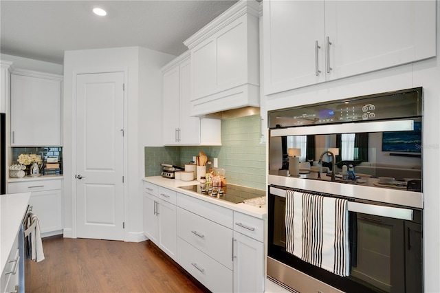 kitchen with white cabinets, light countertops, dark wood finished floors, black electric stovetop, and double oven
