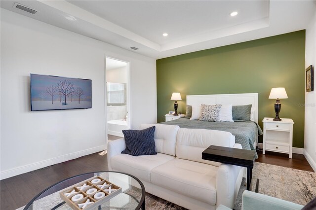 bedroom featuring a tray ceiling, baseboards, visible vents, and wood finished floors