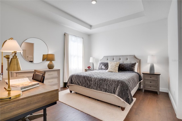 bedroom with hardwood / wood-style floors, baseboards, and a raised ceiling