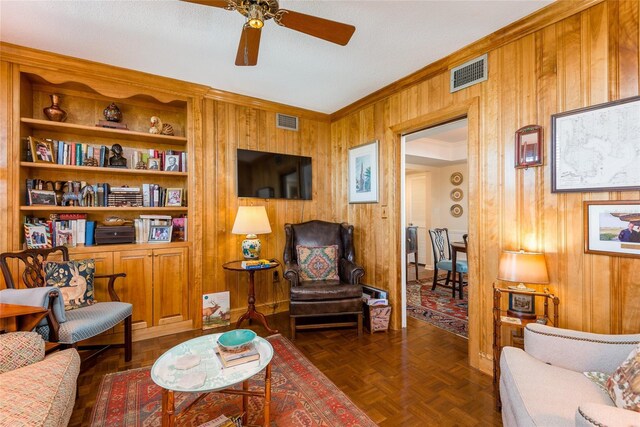 living room featuring visible vents, wood walls, ceiling fan, and crown molding