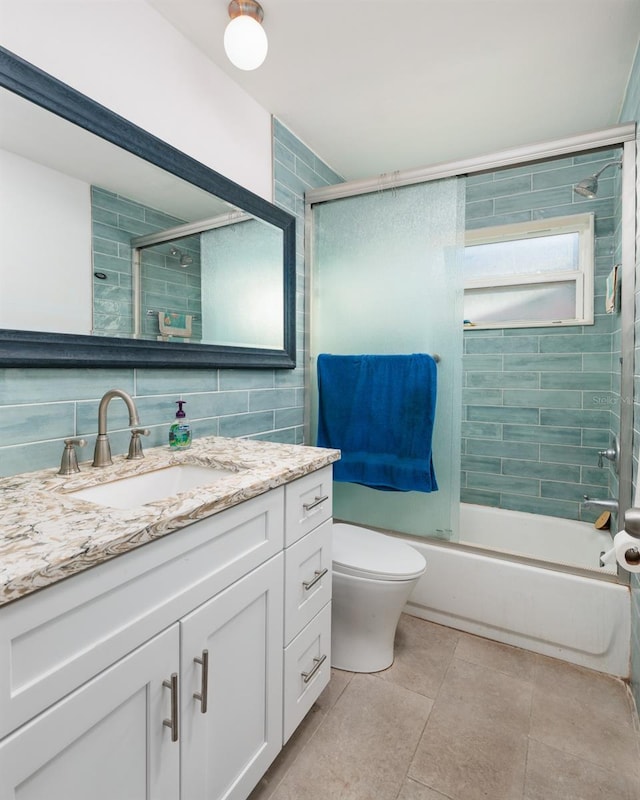 bathroom with tile patterned flooring, vanity, tile walls, toilet, and bath / shower combo with glass door