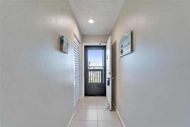 doorway featuring light tile patterned flooring, a textured ceiling, and baseboards