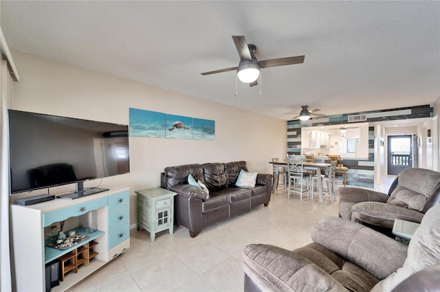 living area featuring light tile patterned flooring, visible vents, ceiling fan, and a textured ceiling