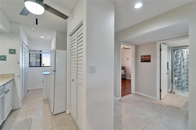 hall with light tile patterned flooring, baseboards, and a textured ceiling