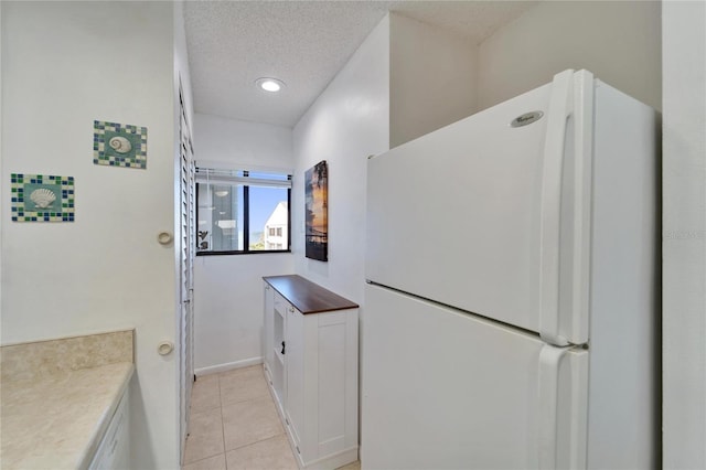 kitchen with freestanding refrigerator, light tile patterned floors, white cabinetry, and a textured ceiling