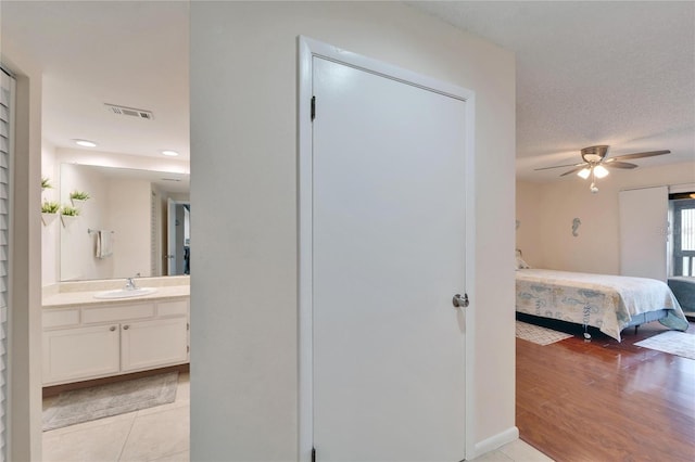 interior space featuring a textured ceiling, a sink, ensuite bath, visible vents, and light wood-style flooring