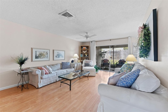 living room featuring light wood-type flooring, baseboards, a textured ceiling, visible vents, and a ceiling fan