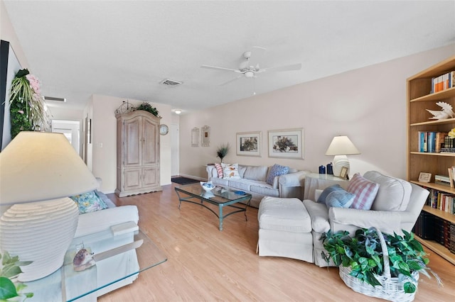 living room featuring light wood-style flooring, baseboards, ceiling fan, and visible vents