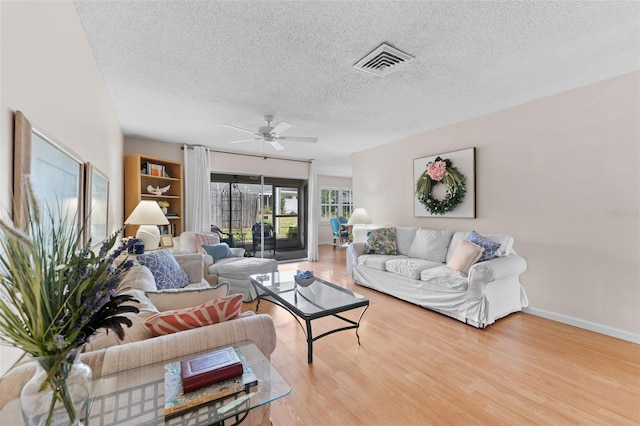 living room with baseboards, a textured ceiling, visible vents, a ceiling fan, and wood finished floors