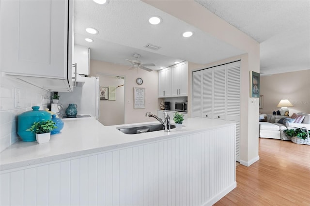 kitchen featuring light countertops, visible vents, a peninsula, stainless steel microwave, and a sink
