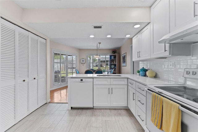kitchen featuring white appliances, under cabinet range hood, a sink, visible vents, and a peninsula