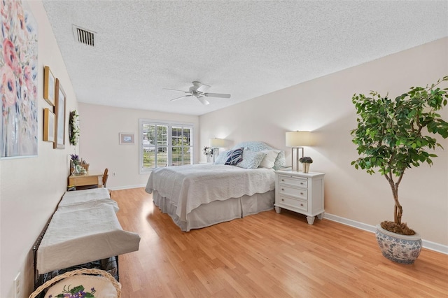 bedroom featuring baseboards, a textured ceiling, visible vents, and light wood finished floors