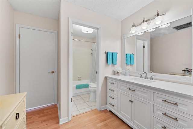 bathroom featuring toilet, vanity, wood finished floors, a textured ceiling, and visible vents