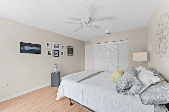 bedroom with baseboards, a textured ceiling, visible vents, light wood-style flooring, and a closet