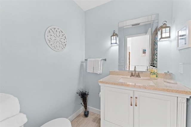 bathroom featuring toilet, vanity, baseboards, and wood finished floors