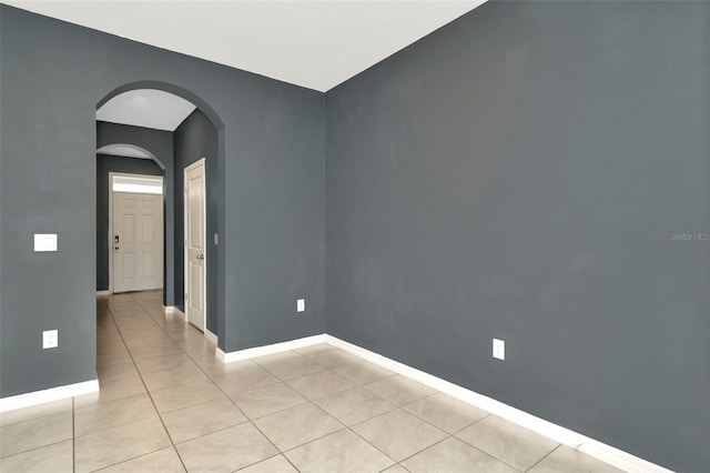 unfurnished room featuring light tile patterned floors, arched walkways, and baseboards