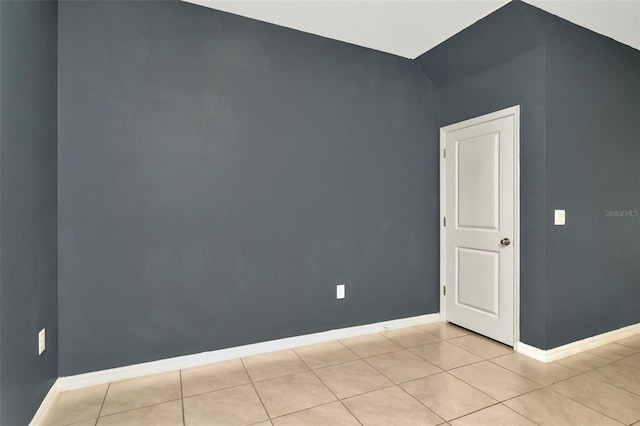 empty room with baseboards, vaulted ceiling, and light tile patterned floors