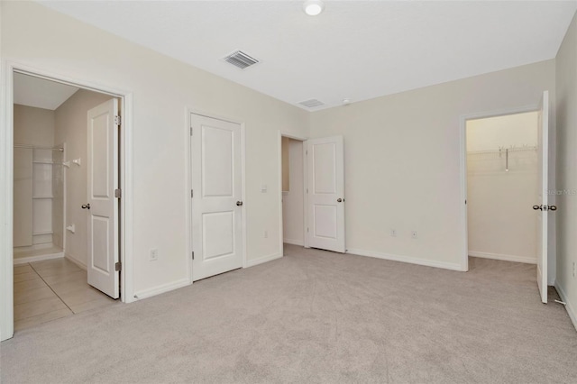 unfurnished bedroom with ensuite bathroom, visible vents, baseboards, light carpet, and a walk in closet