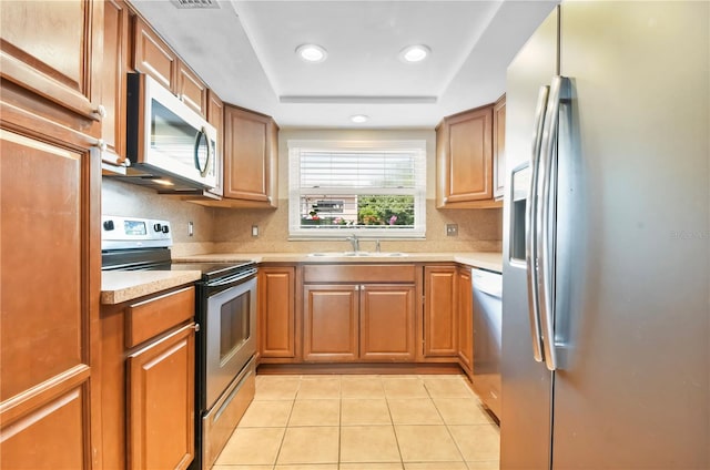 kitchen with a sink, light tile patterned floors, light countertops, backsplash, and appliances with stainless steel finishes