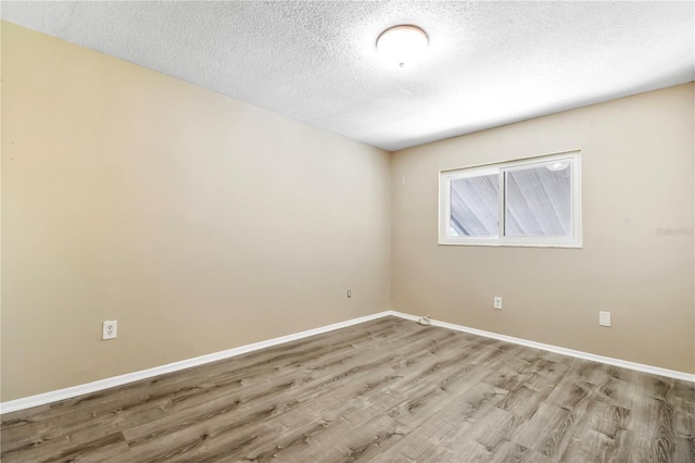 spare room with wood finished floors, a textured ceiling, and baseboards