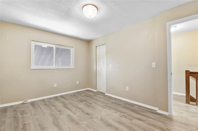 empty room with light wood-style flooring, a textured ceiling, and baseboards