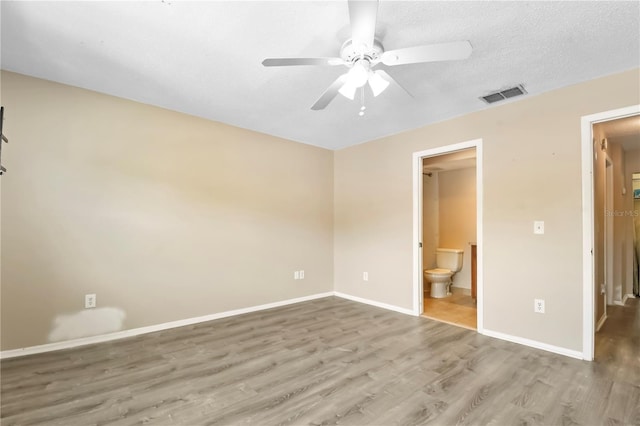 unfurnished bedroom with ensuite bathroom, baseboards, visible vents, wood finished floors, and ceiling fan