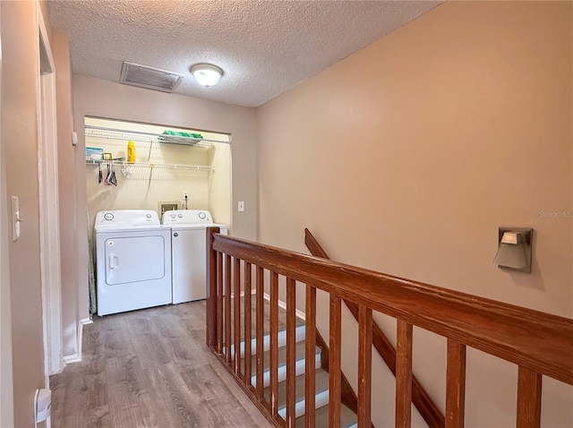 clothes washing area with separate washer and dryer, wood finished floors, a textured ceiling, and visible vents