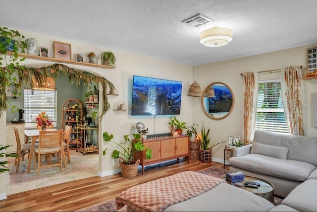 living room with baseboards, a textured ceiling, visible vents, and wood finished floors